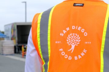 San Diego Food Bank staff member's vest with the Food Bank's logo in front of a line of cars at a food distribution.