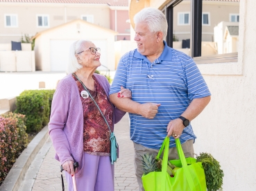 Two seniors linking arms and holding a bag of fresh produce.
