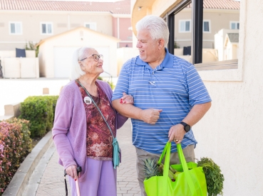 Two seniors linking arms, holding a bag of fresh produce.