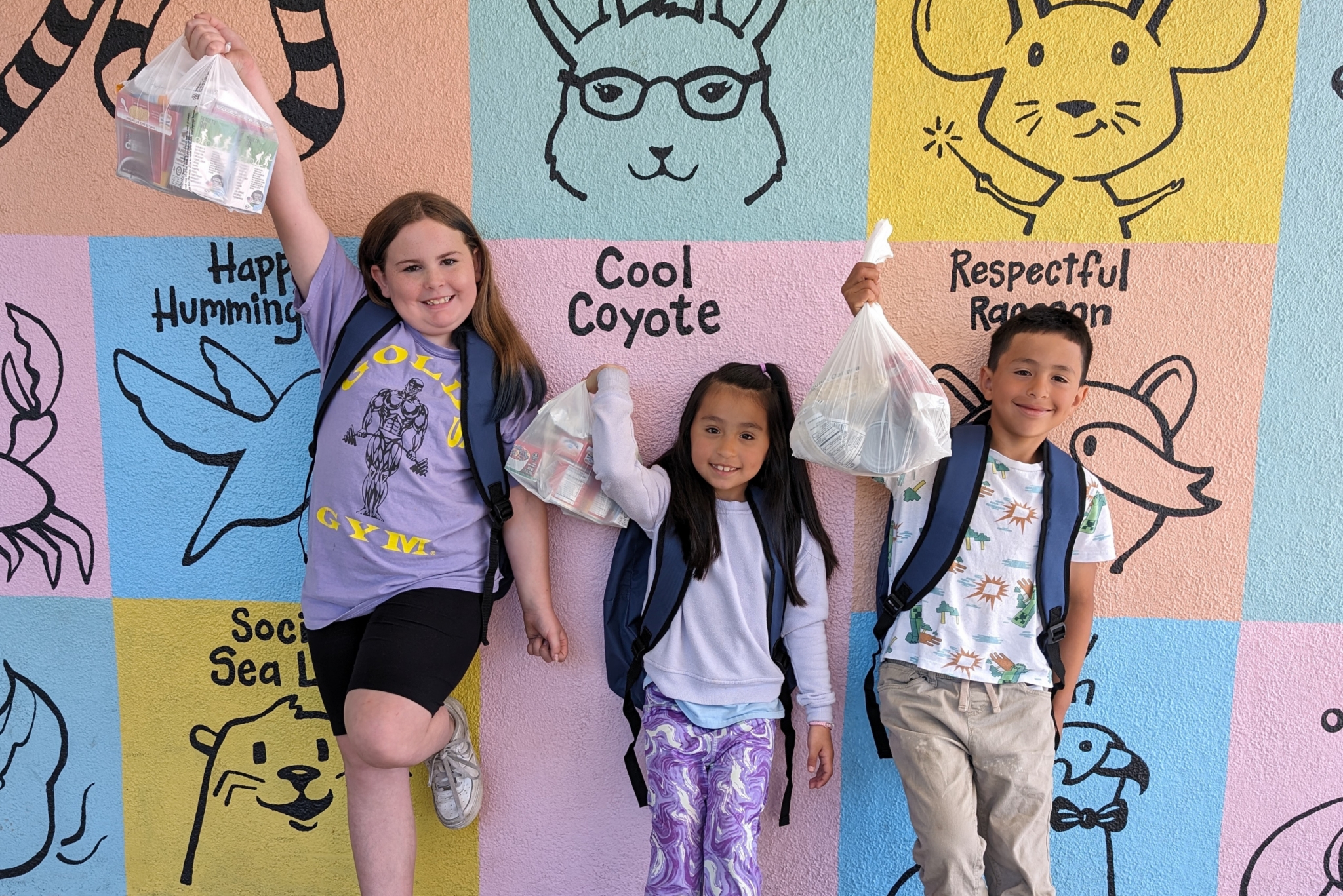 Students on the Food 4 Kids Backpack Program holding up their bag of food.