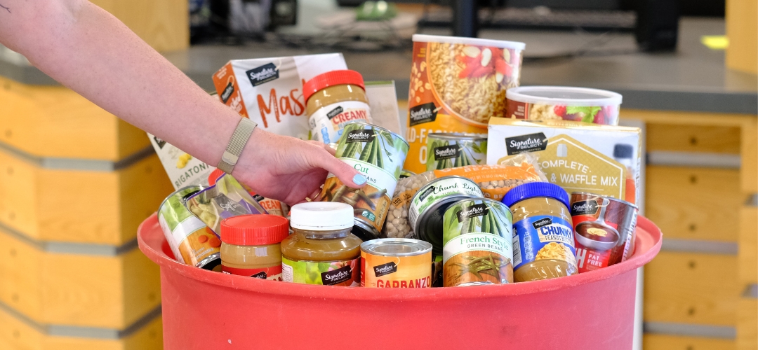 A hand placing food in a red barrel full of nonperishable items.