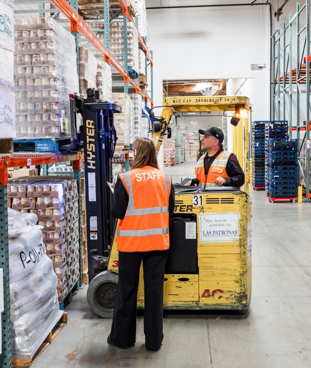 Two staff members in the warehouse and one on a forklift placing food on racking.