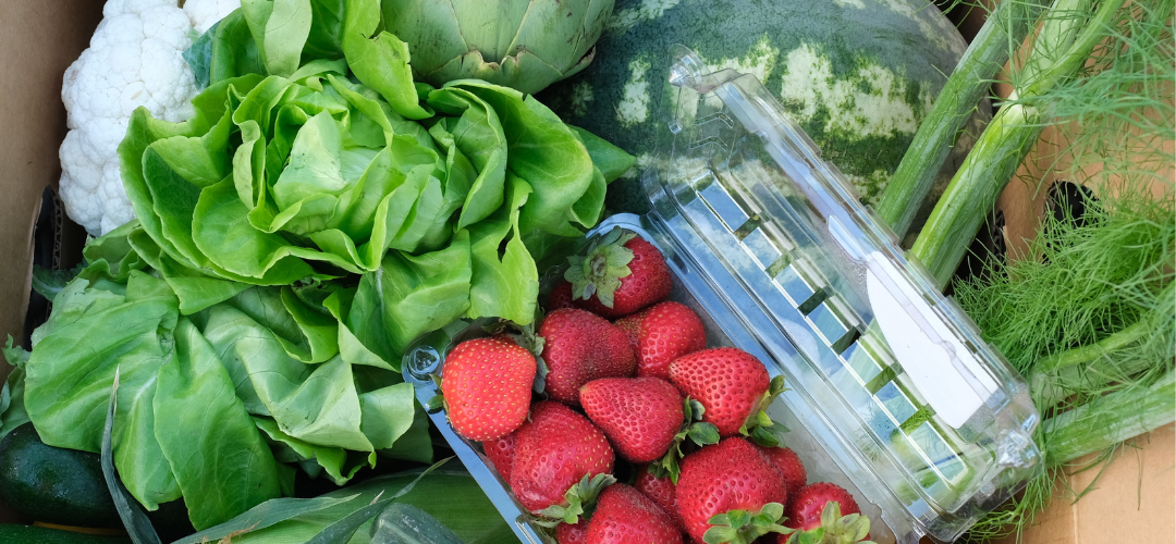 A box of fresh strawberries, lettuce, celery, watermelon, and cauliflower