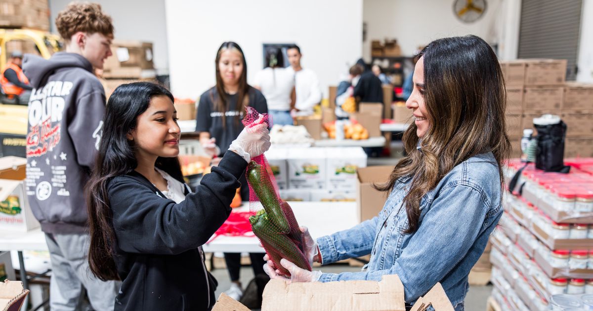 A mother and daughter volunteering by bagging zucchini.