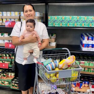 Maria holding her daughter with a cart full of food at our Client Choice Pantry.