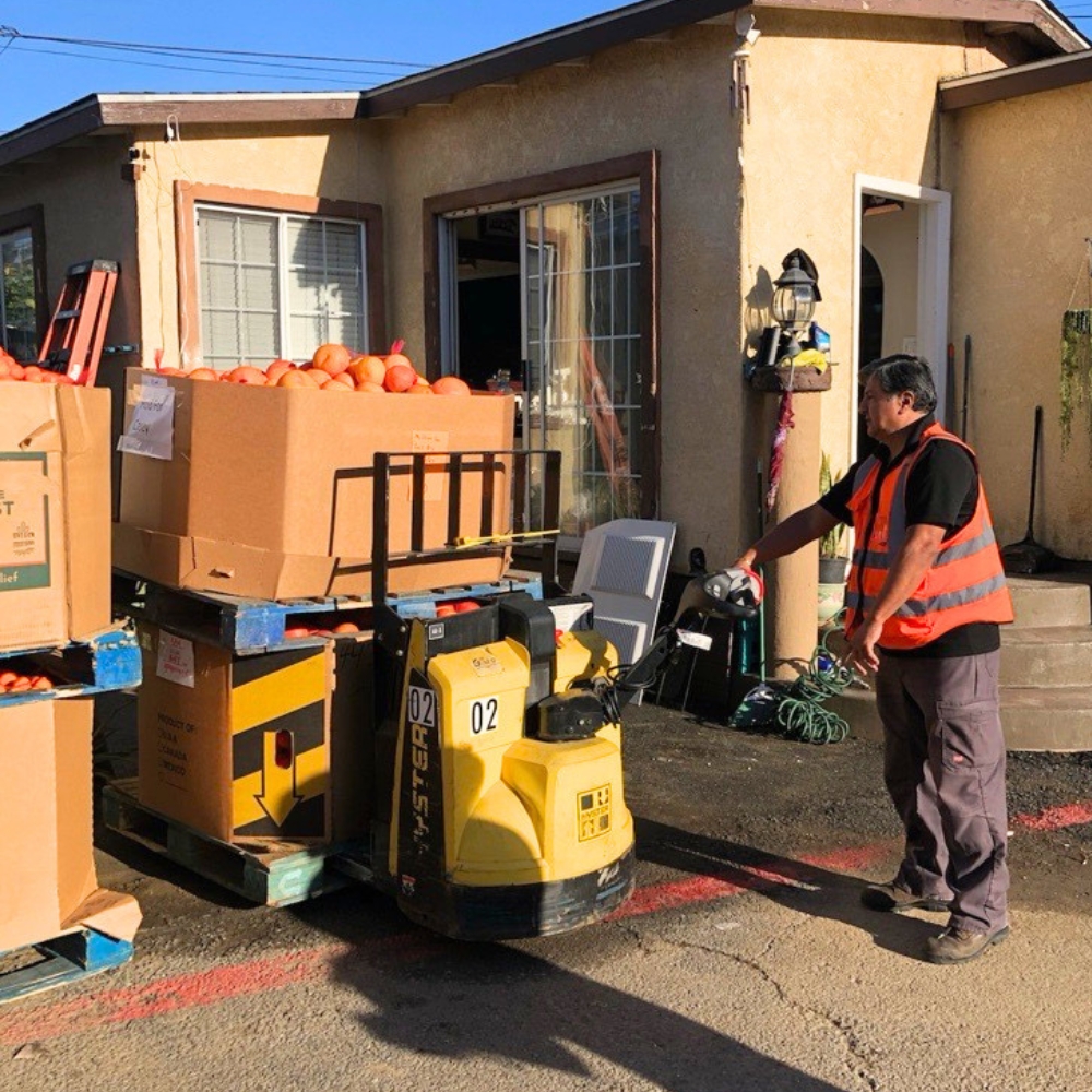 Food Bank staff member moving boxes of fresh produce in a neighborhood affected by flooding